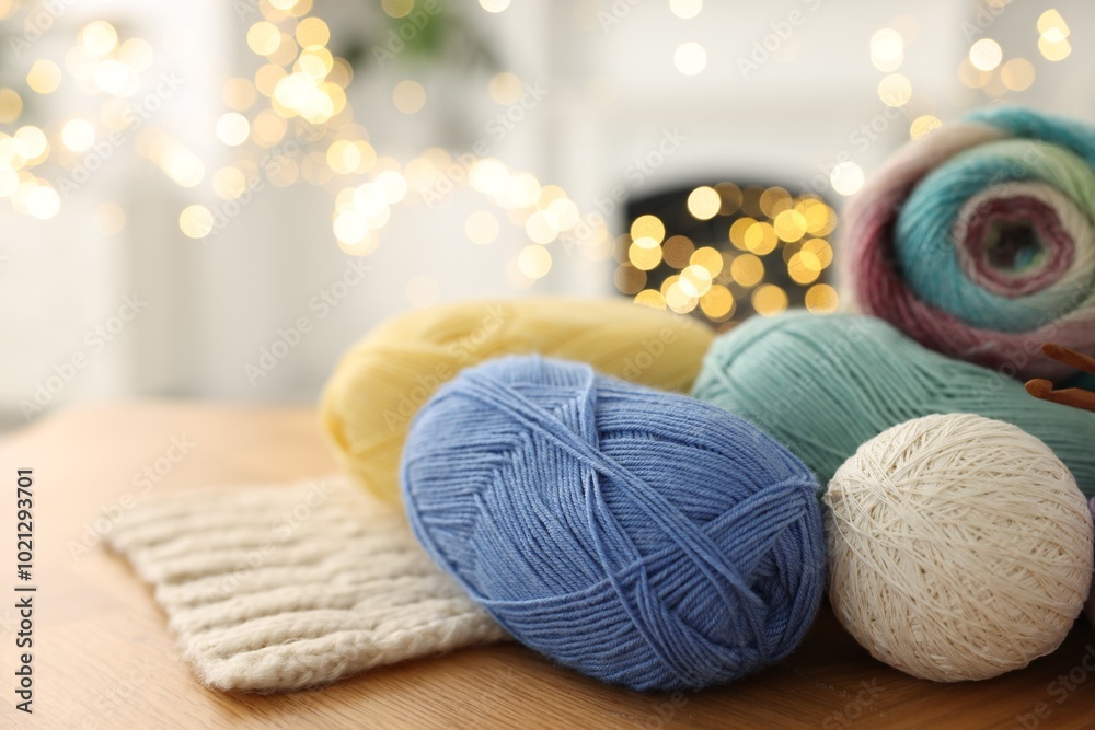 Sticker Colorful yarns and pattern sample on wooden table against blurred lights, closeup. Space for text