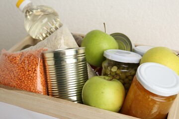 Different products in wooden crate on light background, closeup. Food donation