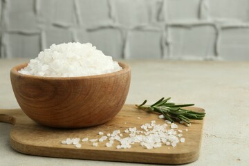 Sea salt in bowl and rosemary on grey table, closeup. Space for text