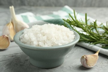 Sea salt in bowl, garlic and rosemary on gray textured table, closeup