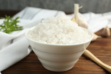 Sea salt in bowl on wooden table, closeup