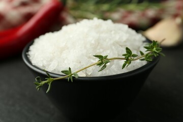 Sea salt and thyme in bowl on dark gray table, closeup