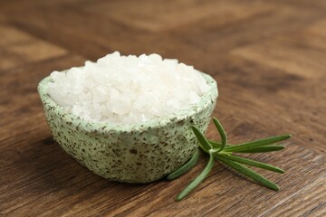 Sea salt and rosemary in bowl on wooden table, closeup