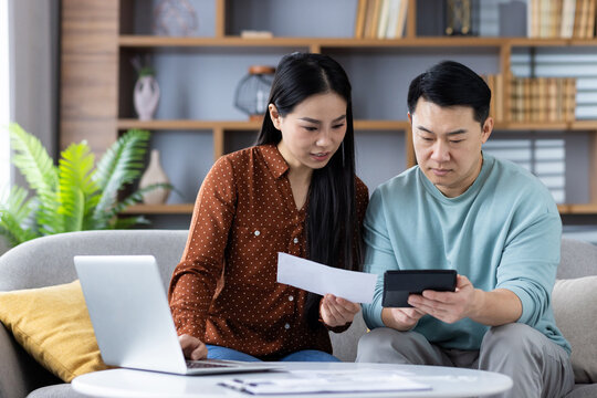 Couple managing finances at home using calculator and laptop, focusing on budgeting and expense tracking for responsible financial planning, teamwork, and collaboration.