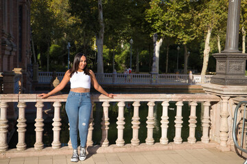 Moroccan woman, young, beautiful, brunette, wearing white top and jeans, looking at camera, leaning on a stone railing. Concept of ethnicity, diversity, femininity, beauty.