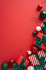 Stylish vertical Christmas presents with green bows and festive decorations on a red surface create a cheerful holiday atmosphere