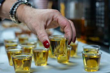 Woman is picking up a shot glass filled with alcohol from a tray of similar drinks at a party. Selective focus