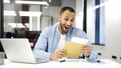 Excited joyful african american businessman reading letter with great news sitting at workplace in business office. Black man worker is celebrating success, happy to receive positive good notification