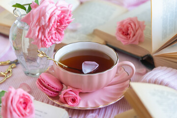 A cup of aromatic tea, a book and a rose on the table.
