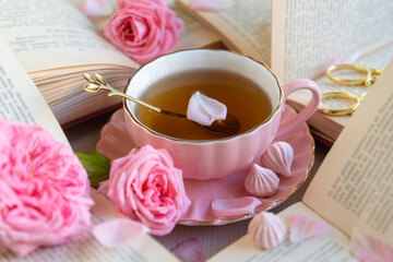 A cup of aromatic tea, a book and a rose on the table.