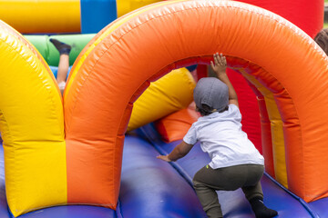 Boy in a baseball cap energetically climbs an inflatable structure at a colorful outdoor birthday party, enjoying the fun and active play