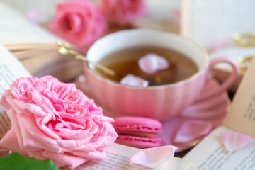 A cup of aromatic tea, a book and a rose on the table.
