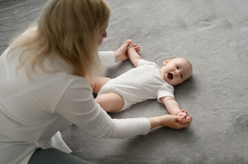 Caring mom doing baby gymnastics for newborn. Mom doing morning exercises for happy baby lying on bed, bending and unbending baby arms, close-up. Children health, baby massage for children. Infancy