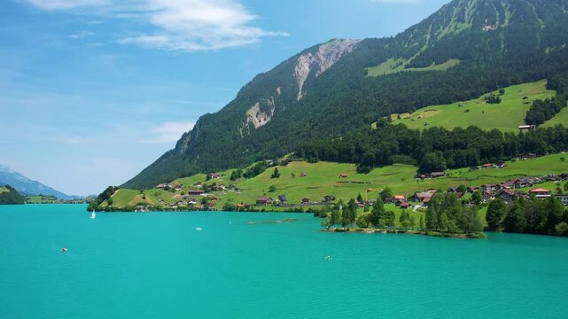 Drone footage of turquoise clear lake Lungern or Lungerersee in Switzerland in summer sunny day with village and green meadow