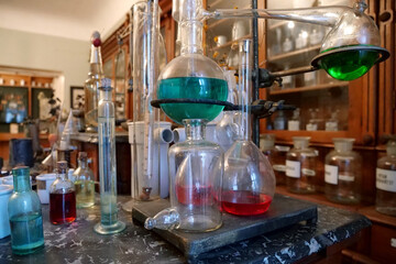 Chemistry beakers and flasks with colorful liquids lies on table in old pharmacy