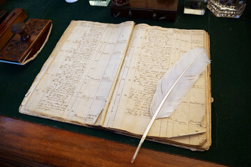 Old recipe book and white feather pen for writing lies on table