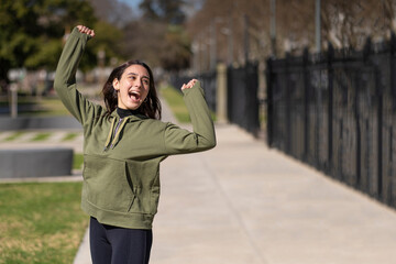 Fototapeta premium Young girl wearing sportswear celebrates in the park smiling screaming and with arms raised