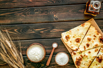 Focaccia ingredients. Wheat ears, flour, oil near bread on dark wooden background top-down copy space