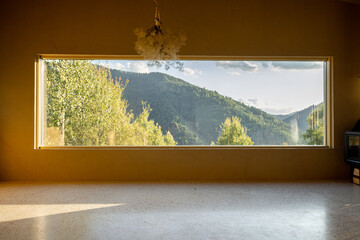 Large panoramic window offering a stunning view of lush green hills and forests. Natural light fills the room, creating a peaceful atmosphere that connects the interior to the beauty of nature