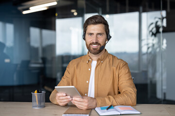 Professional man wearing headset using tablet in modern office shows remote work technology....