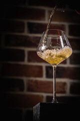Pouring white wine into the glass against Brick wall bottom view