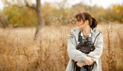 dreamy girl standing alone in an autumn park, wrapped her arms around the backpack. People,...