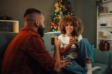 Young couple relaxing on sofa drinking coffee by christmas tree