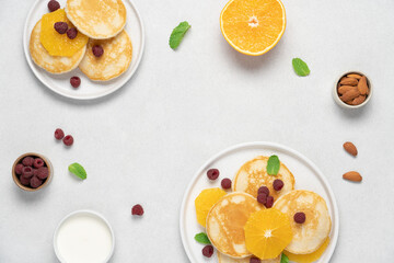 Pancakes with orange and raspberries in plate top view on white background with copy space. Morning...