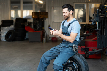 Mechanic taking a break on phone in auto shop after changing seasonal tires