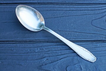 one  shiny steel iron clean empty gray oval traditional old patterned handle spoon lies on wooden black table