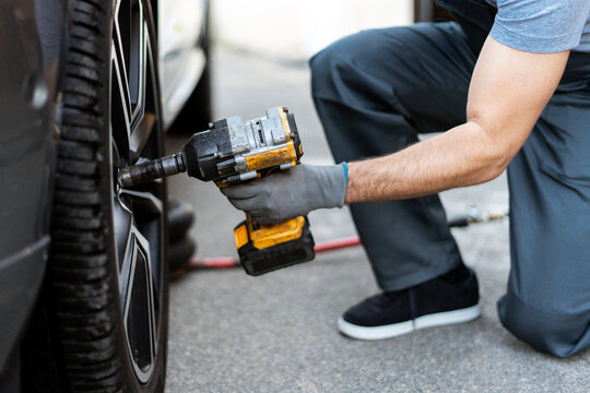 Mechanic changing car tire using battery powered impact wrench