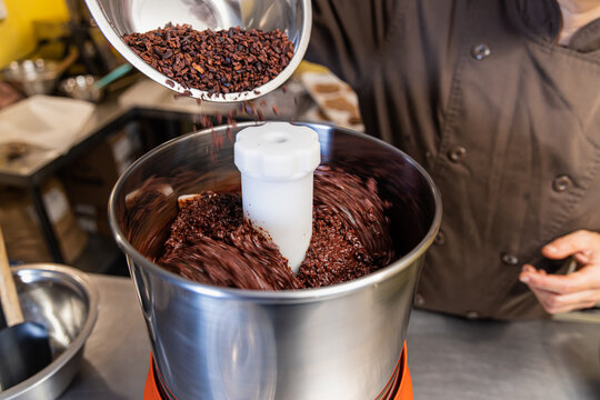 Chocolatier adding cocoa nibs into a professional melanger machine for chocolate making. Selective focus