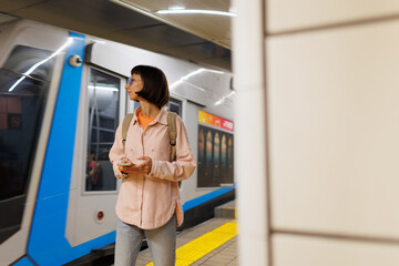 Fototapeta premium girl waiting for train. girl in subway. Young girl in stylish clothes with backpack using smartphone in subway.