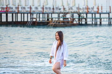 Beautiful young woman at beach looking at camera. Happy latin girl in white bikini smiling. Portrait of young tanned woman relaxing on beach with copy space and sea in background.