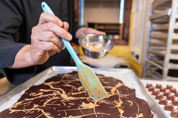 Chocolatier is spreading cream over a layer of dark chocolate on a baking sheet to make a delicious dessert. Selective focus
