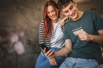 Happy young couple buy online on mobile phone with credit card at home