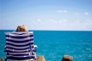 Fototapeta premium A girl sits on a sun lounger on the seashore. Holidays by the sea.