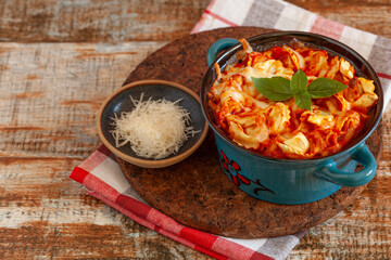 Tortellini bake with mozzarella and parmesan cheese, tomato sauce in baking dish on dark wooden table