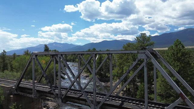 Inactive railroad bridge over the Arkansas River in Colorado. Flight rises up and over the bridge showing the valley, river and mountains beyond.