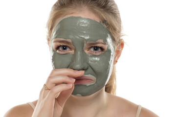 Disappointedl funny young woman smelling her facial green mud mask on her face. Skin care and treatment, spa, natural beauty and cosmetology concept