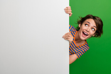 Photo portrait of pretty young girl hide behind look white wall dressed stylish striped outfit isolated on green color background