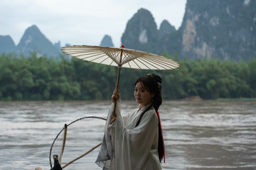 Beautiful young Hanfu girl with umbrella posing on a bamboo raft in Xingping, China. Close up