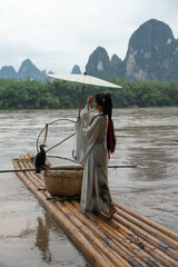 Woman in Hanfu attire holds an umbrella while standing on a bamboo raft in Xingping, China