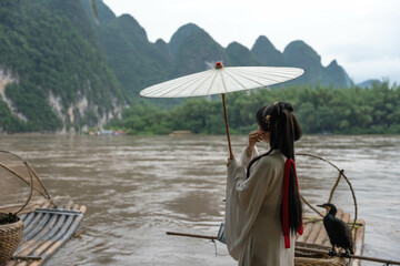 Han Dynasty girl with long hair and an umbrella next to a cormorant on the Li River. Xingping, China