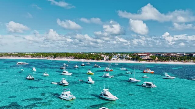 White yachts on the background of the coast with a hotel. Boats at the tropical sea coast with a white sandy palm beach on a sunny day. Summer vacation in the Dominican Republic.