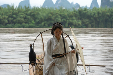 Chinese Hanfu girl with umbrella openning arms on bamboo raft in Li River. Vertical