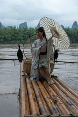 Hanfu girl with umbrella on bamboo raft in Xingping posing with cormorants