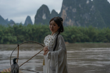 Hanfu girl balances on a bamboo raft with round fan and Cormorant during a photo session. Xingping