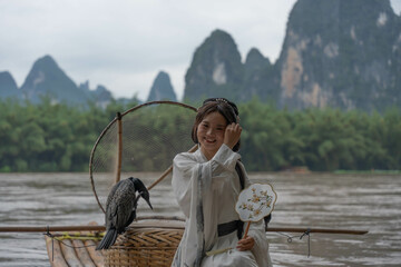 Hanfu girl posing on bamboo raft with Cormorant on Li River