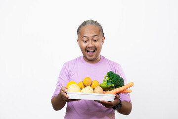curly-haired Asian adult male carrying a tray of fresh vegetables while pointing at it, healthy and nutritious fresh vegetables eating campaign, healthy lifestyle